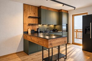Une cuisine moderne avec un îlot central en bois, des meubles de couleur sombre et une vue sur l’extérieur.