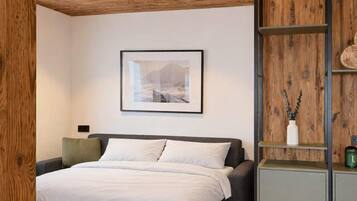 Un dormitorio con una cama, un cuadro en la pared y una repisa de madera con un jarrón.