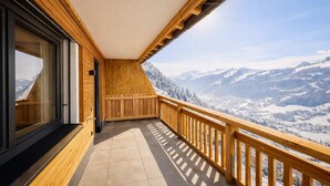 Ein Balkon mit Holzwertung, Blick auf verschneite Berge und einen klaren Himmel.