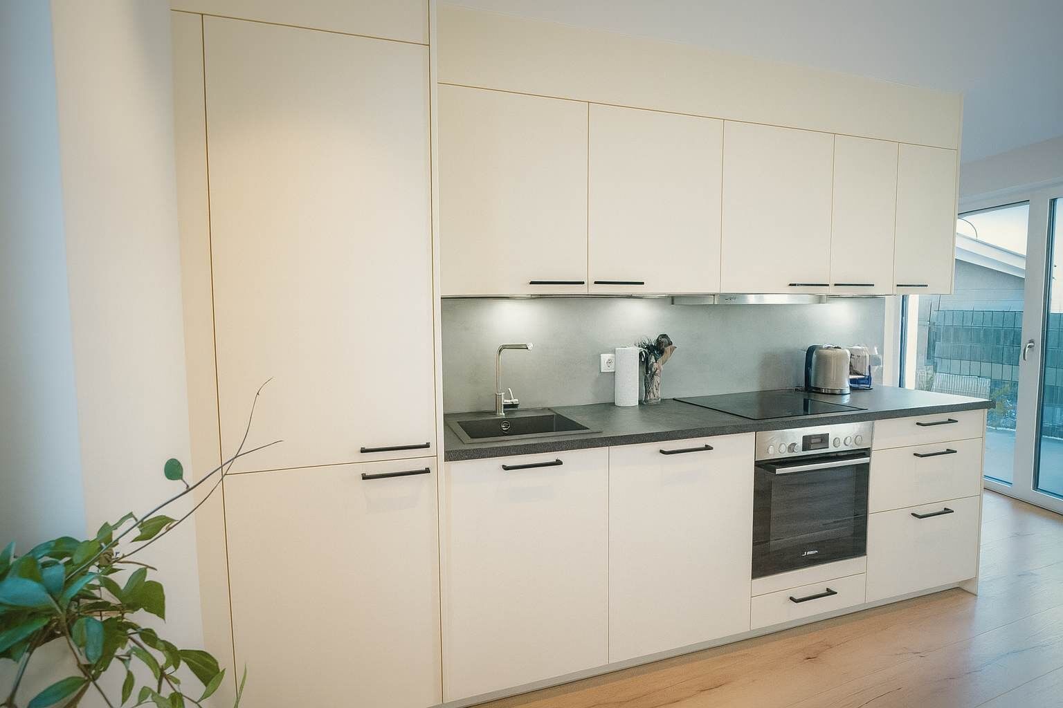 Una cocina moderna con armarios blancos, estufa de acero inoxidable y encimera negra.