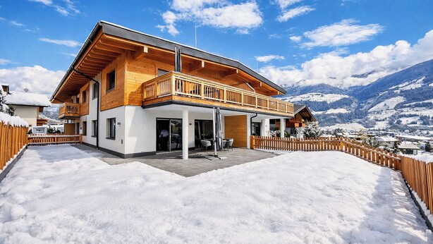 Ein modernes Chalet mit Holzfassade, einem Balkon und Blick auf schneebedeckte Berge.