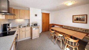 Cocina compacta con microondas, estufa y lavamanos, una mesa de comedor de madera con sillas y un banco.