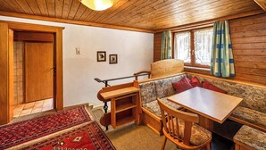 Un interior de cabaña acogedor con techo de madera, una mesa de comedor, un banco y una ventana con cortinas.