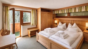 Un dormitorio con una cama grande, cabecera de madera, mesitas de noche, un escritorio y una ventana con cortinas.