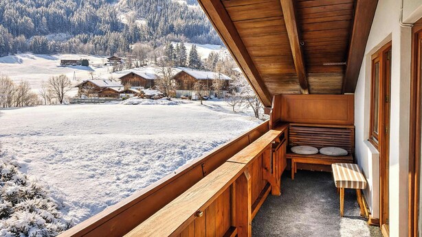 Un balcón de madera con vistas a un paisaje nevado y casas.