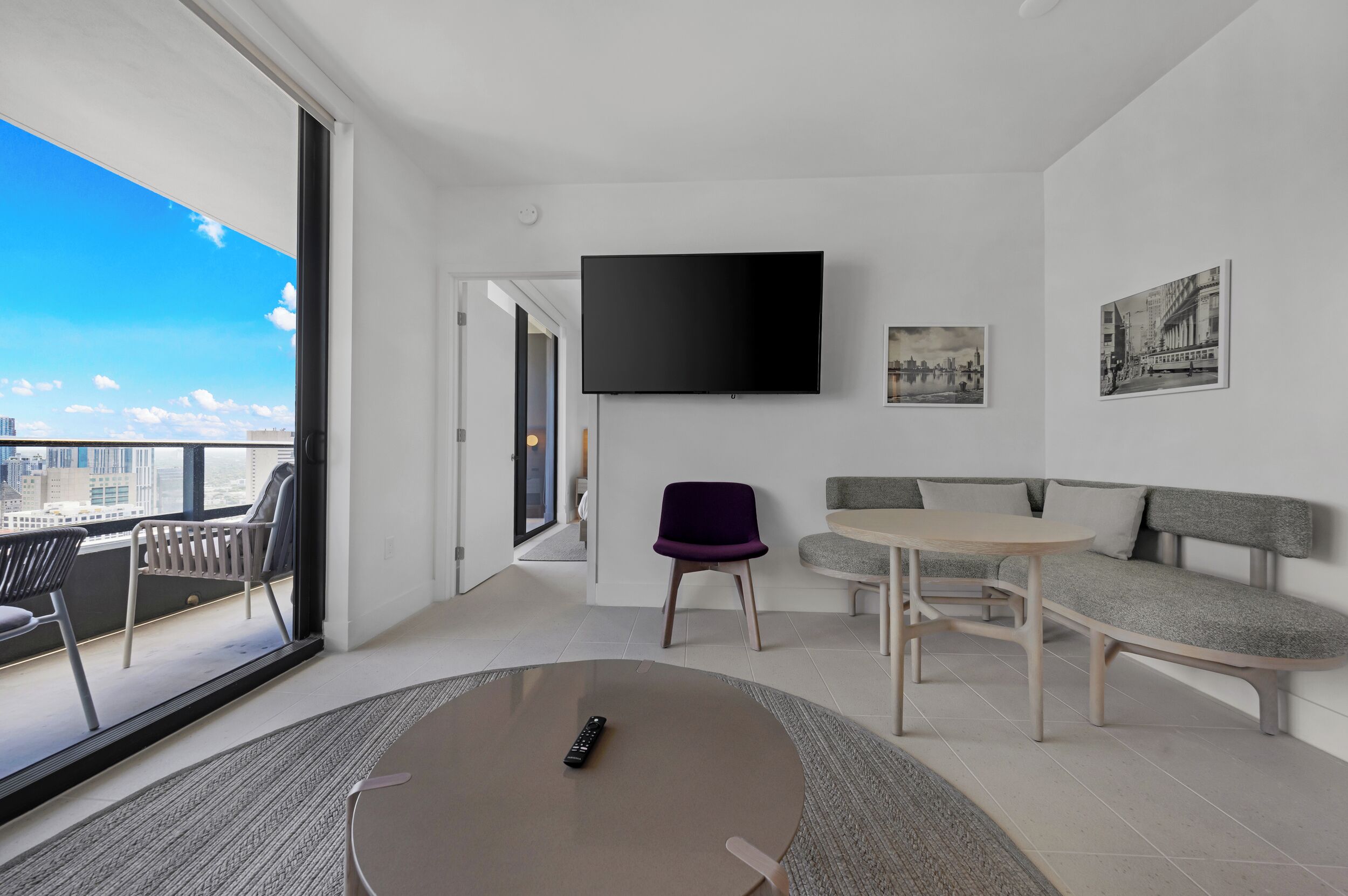 A modern living room with a sofa, a table, a chair, a TV, and a balcony with a city view.
