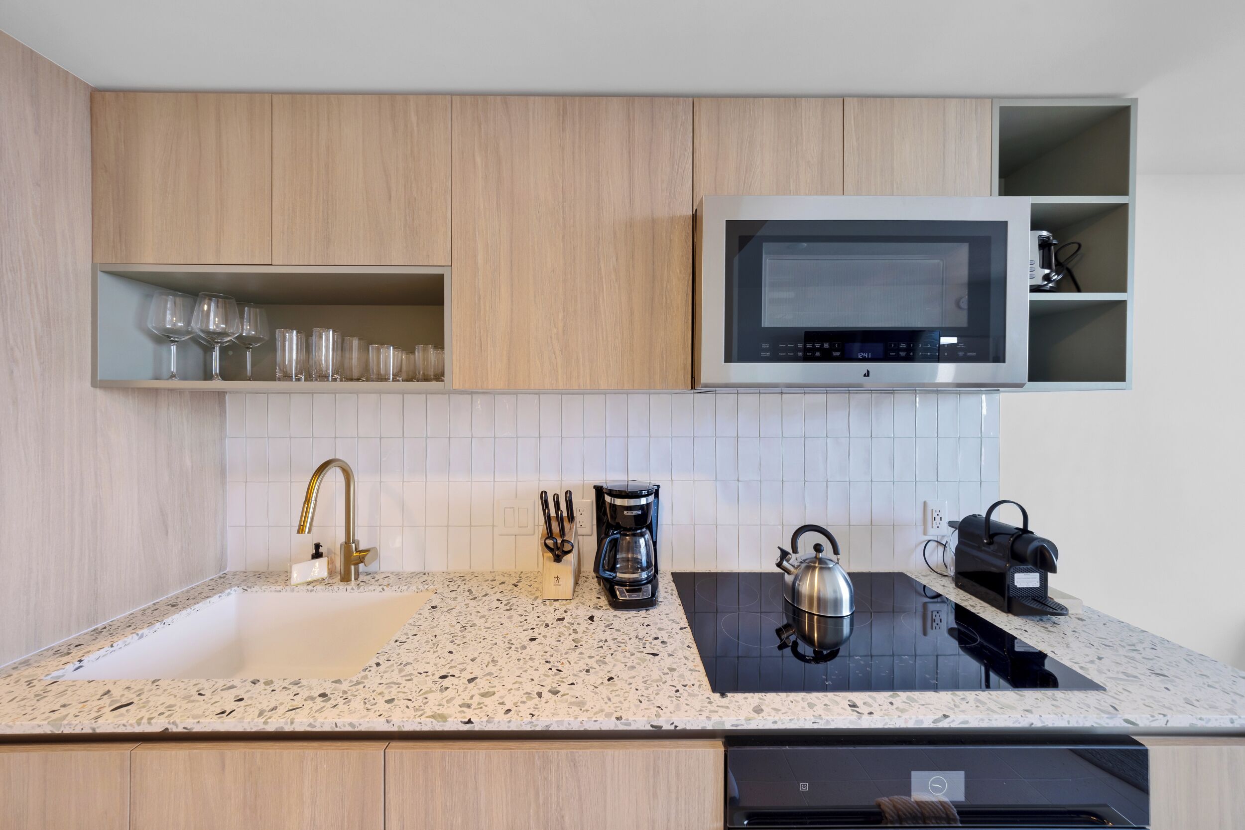A modern kitchen with a built-in microwave, a kettle, and a coffee maker on the countertop.