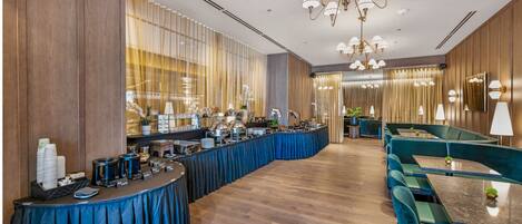 Eine moderne Hotelhalle mit einem gebogenen Buffet, grünen Polstersesseln und einer Kristallleuchtre.