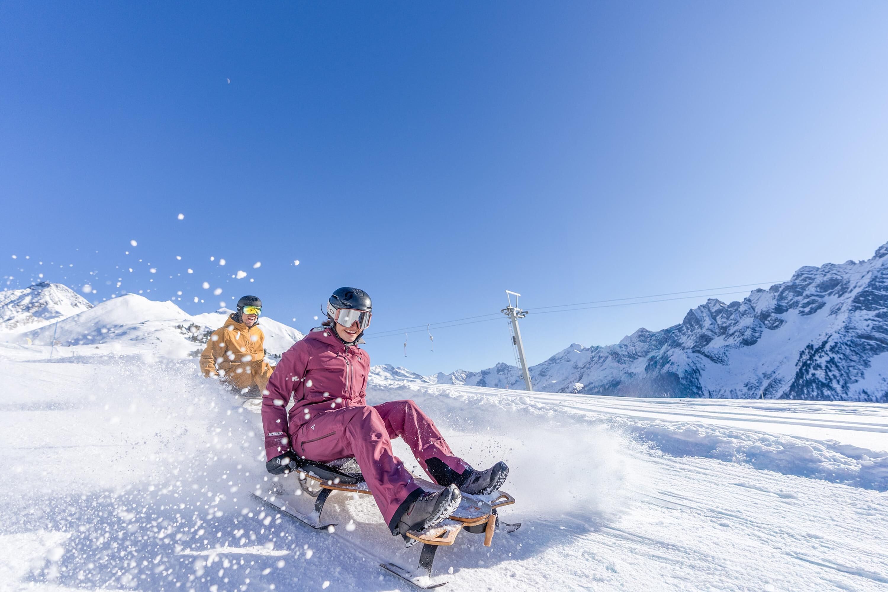 A snow-covered slope with a person in a purple outfit sitting on a sled.