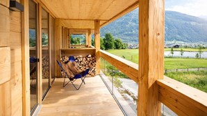 Ein Holzbalkon mit Blick auf einen See und Berge, ein Stuhl und ein Holzstapel.
