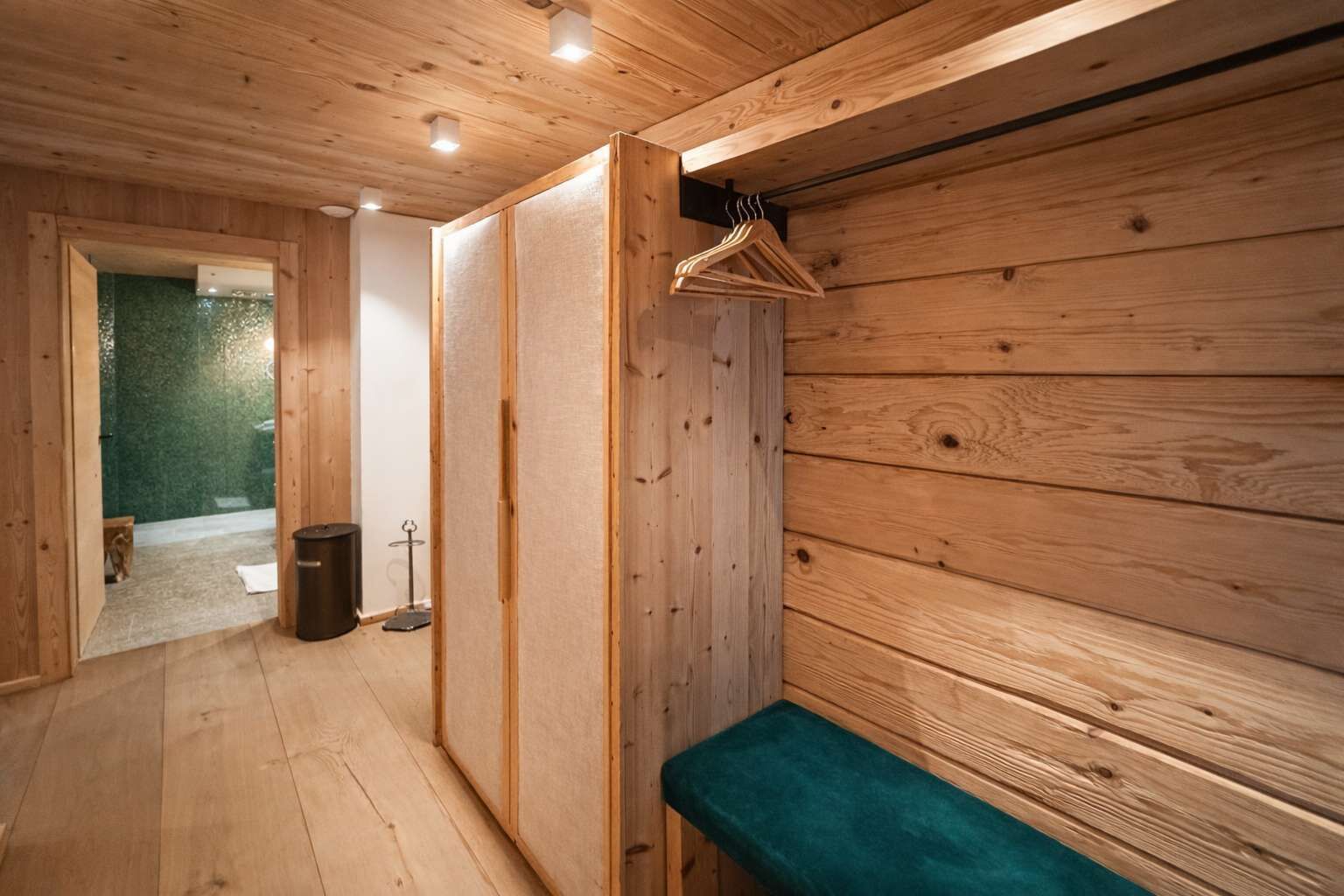 Ein Zimmer aus Holz mit einer Bank, einem Kleiderständer und einer Tür zu einer Grünfläche.