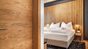 A bedroom with a wooden headboard, a bed with white bedding, a small bedside table, and a wall-mounted light. - CHEZ NOUS – Balcony & Mountain View (Fügen)