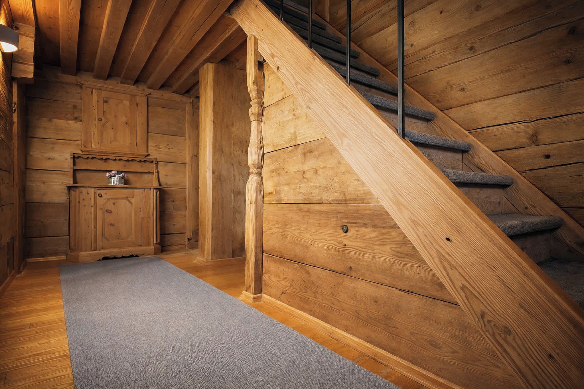 A wooden staircase leading to a loft bedroom with a built-in wooden wardrobe and a small shelf.