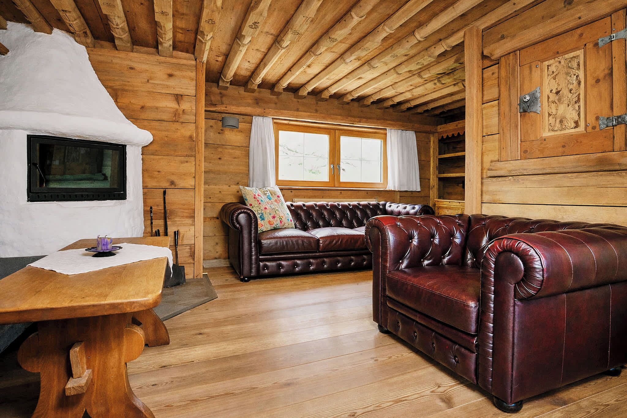 Interno di una baita in legno con camino, divano in pelle e tavolo da pranzo in legno.