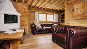 Interno di una baita in legno con camino, divano in pelle e tavolo da pranzo in legno.