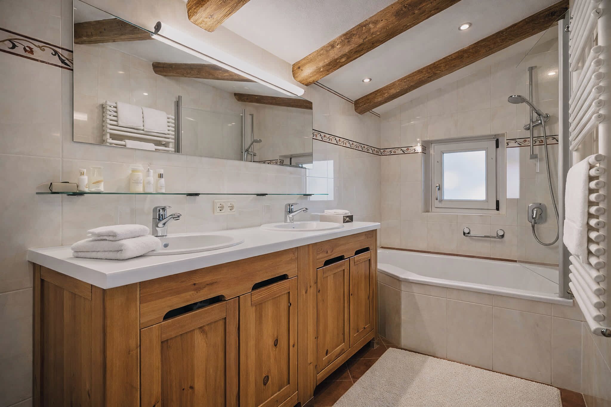 Un baño con armarios de madera, lavamanos doble, un espejo grande y una bañera.