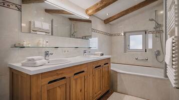 Un baño con armarios de madera, lavamanos doble, un espejo grande y una bañera.