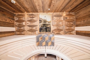 Een houten sauna met een centrale bank, geometrische wandpatronen en een ingelijst schilderij.