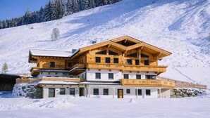 A multi-story wooden chalet with balconies, set against a snowy mountain backdrop. - BEIM LOIS Edelweiss – with Sauna Access (Gerlos)