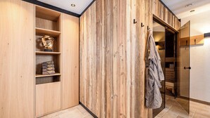 A wooden wardrobe with shelves, a robe hanging, and a mirrored closet door. - BEIM LOIS Edelweiss – with Sauna Access (Gerlos)