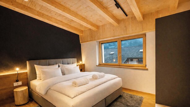 Quarto com cama, mesas de cabeceira, janela e teto de madeira.