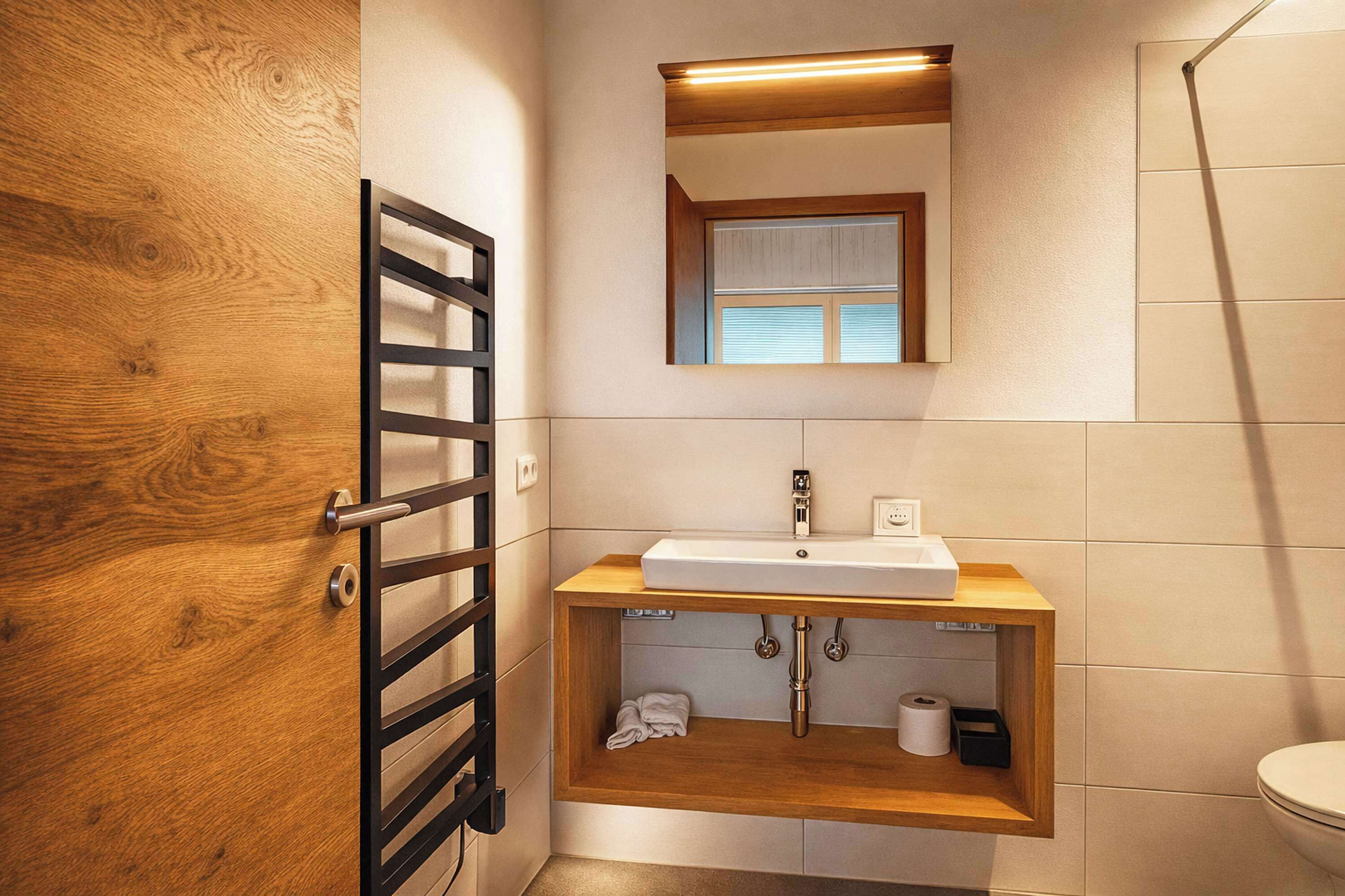 A bathroom with a wooden door, a towel rack, a sink with a wooden countertop, a mirror above the sink, and a toilet.