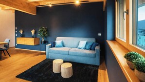 Uma sala de estar moderna com um sofá, duas mesas redondas de madeira, um tapete preto e teto de madeira.