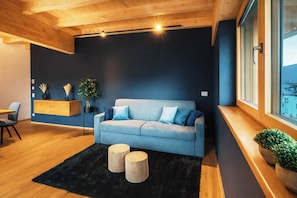 Ein modernes Wohnzimmer mit einer Couch, zwei runden Holztischen, einem schwarzen Teppich und einer Holzzieldecke.