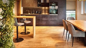 A modern kitchen with dark cabinetry, a wooden dining table, and two bar stools. - ViVaZILARE – Design Loft with Terrace (Fügen)