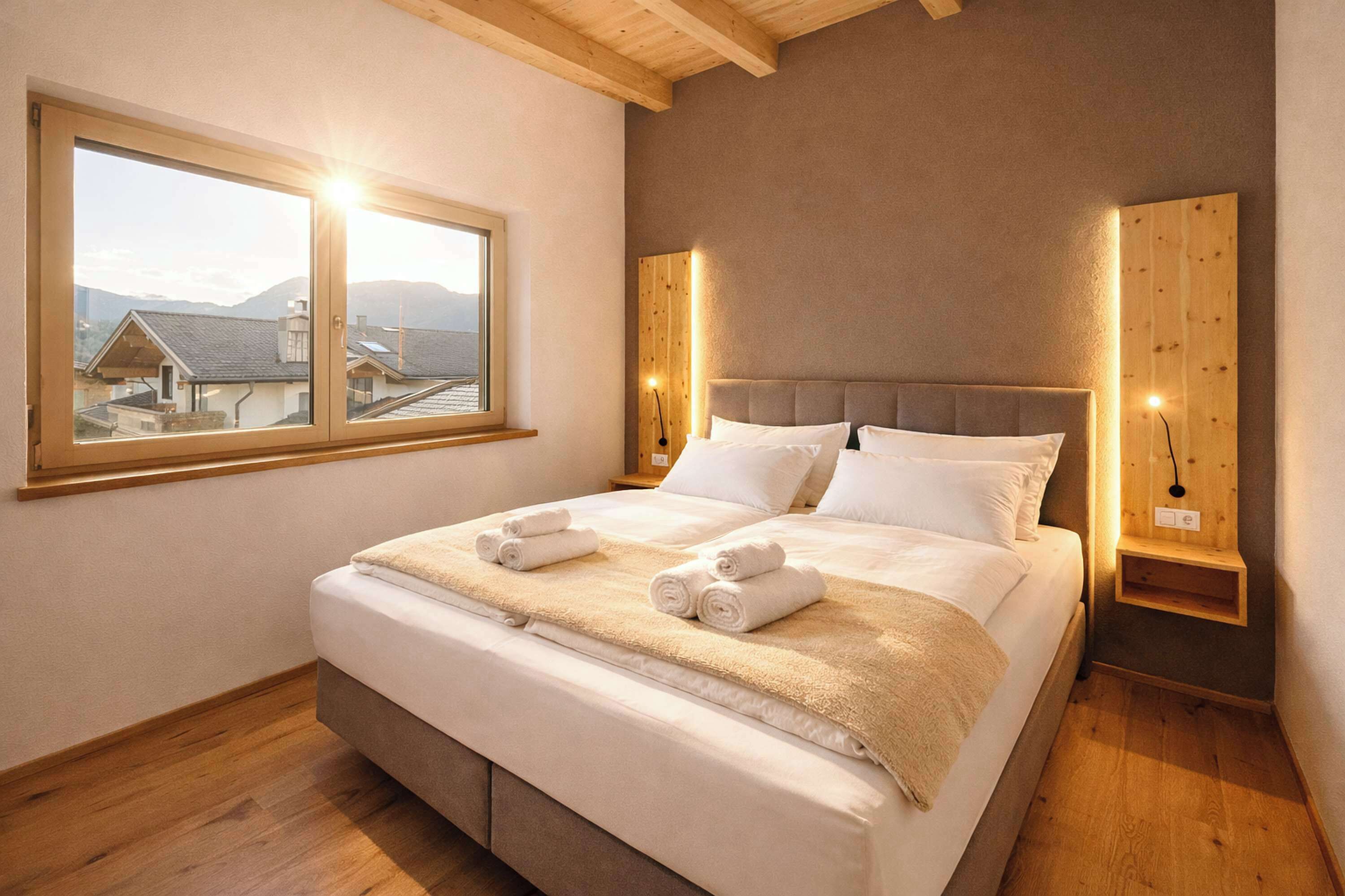 A bedroom with a large bed, a window with a view, wooden wall paneling, and a bedside table.