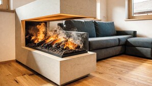 A modern living room with a built-in fireplace, a grey sofa, and a window with blinds. - ViVaZILARE – Design Loft with Terrace (Fügen)