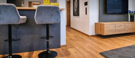 A modern kitchen with two bar stools, a wooden cabinet, and a flat-screen TV on the wall.