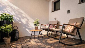 En træterrasse med to gyngestole og et lille bord, omgivet af plantekasser.