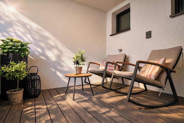 A wooden deck with two rocking chairs and a small table, surrounded by potted plants.