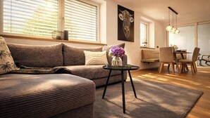 En moderne stue med en sofa, et lille rundt bord med en vase, og et spiseområde med stole og bord.