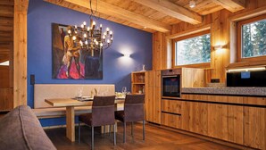 A modern kitchen with wooden cabinetry, a dining area with a table and chairs, and a large painting on the wall. - GOLF Suite – Penthouse, Balcony & Sauna Access (Kleinboden)