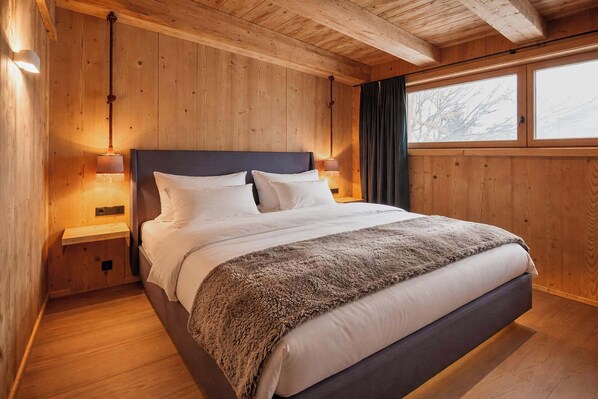 A wooden-paneled bedroom with a bed, nightstands, and a window. - GOLF Suite – Penthouse & Sauna Access (Kleinboden)