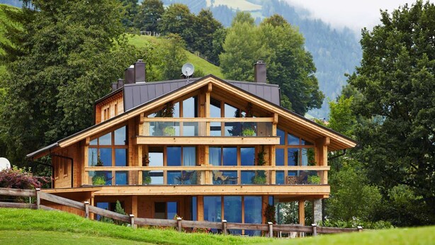 A two-story wooden chalet with large windows, a balcony, and a scenic mountain backdrop. - GOLF Suite – Penthouse, Balcony & Sauna Access (Kleinboden)