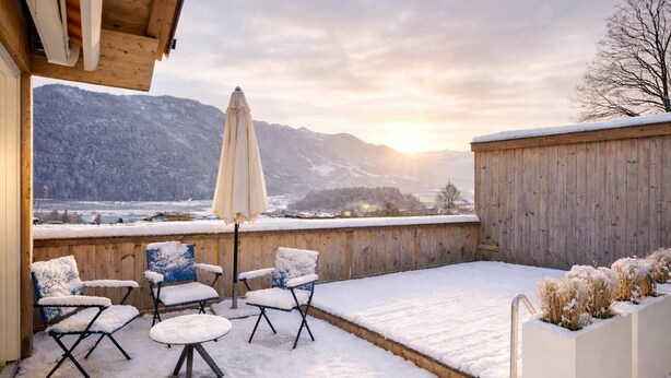 Eine mit Schnee bedeckte Terrasse mit Sitzgelegenheit und Blick auf Berge.