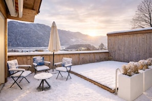 A snow-covered patio with outdoor seating and a view of mountains.