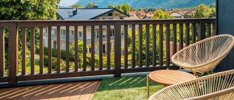 A balcony with a wooden railing, two wicker chairs, and a view of a mountainous landscape.