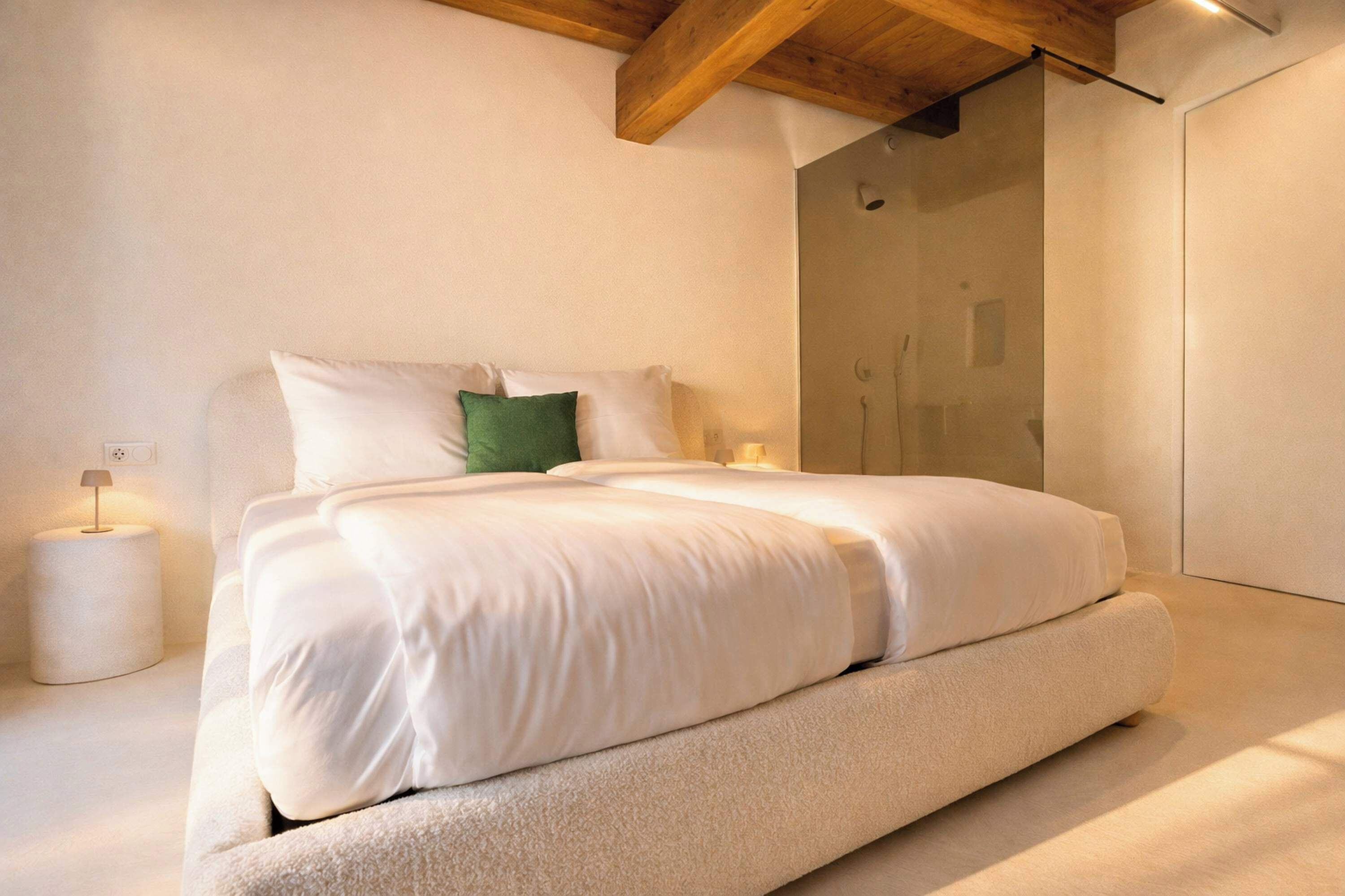 Quarto moderno com cama grande, mesa de cabeceira, travesseiro verde e chuveiro fixado na parede.