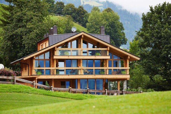 Eine zweistöckige Holzhütte mit großen Fenstern, einem Balkon und einer malerischen Bergkulisse.