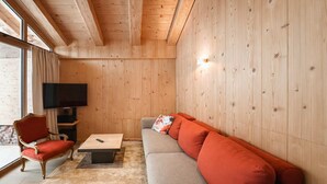 Ein Zimmer mit Holzwänden, einer Couch, einem roten Sessel, einem Couchtisch und einem Fernseher.