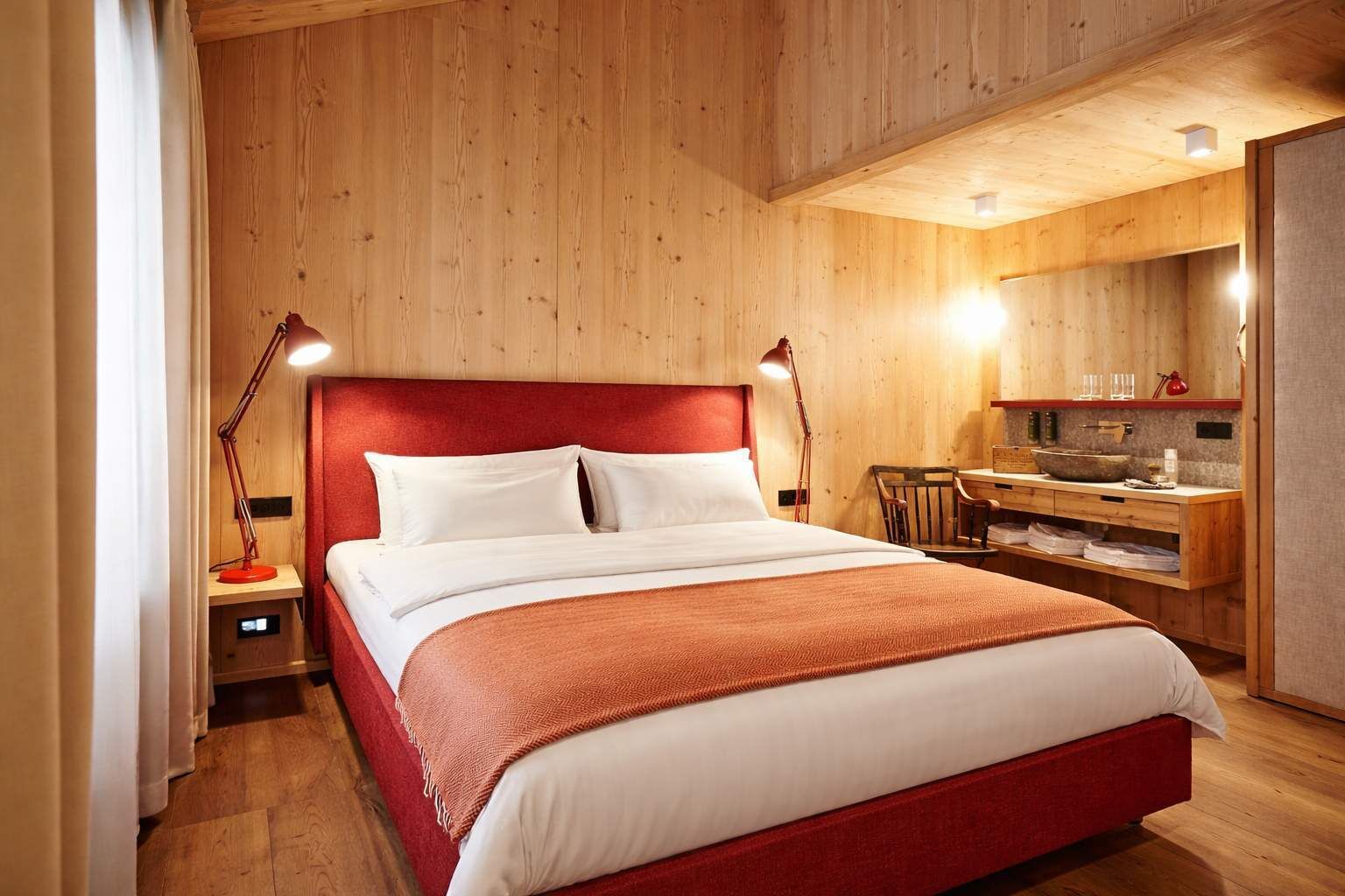 Una stanza con rivestimenti in legno, un letto, comodini, una scrivania e uno specchio.