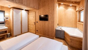Ein Zimmer in einer Holzhütte mit einem Bett, einem Fernseher, einem kleinen Waschbecken und einer Badewanne.