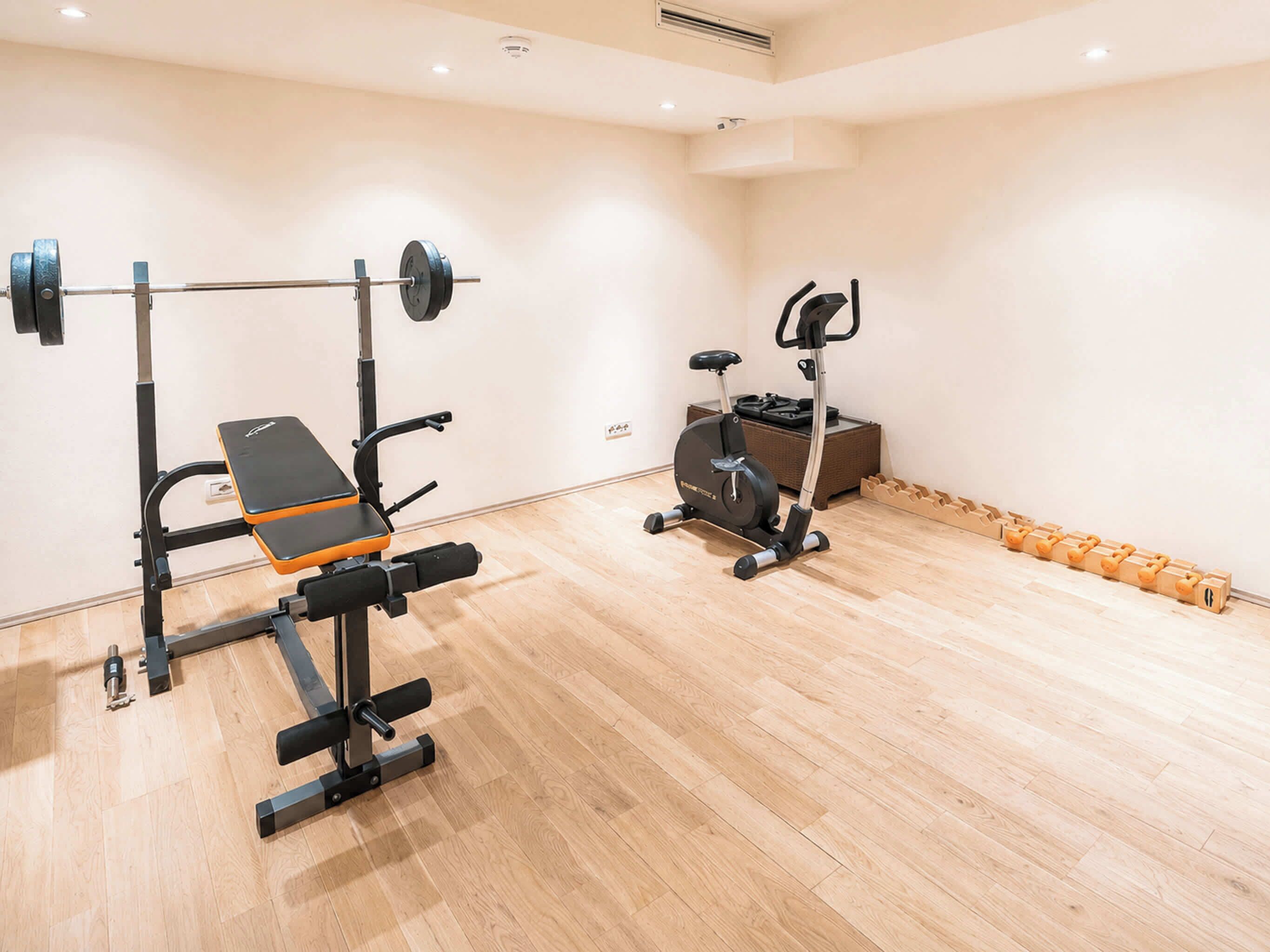 A gym with a bench press, a squat rack, an elliptical, and a set of dumbbells.