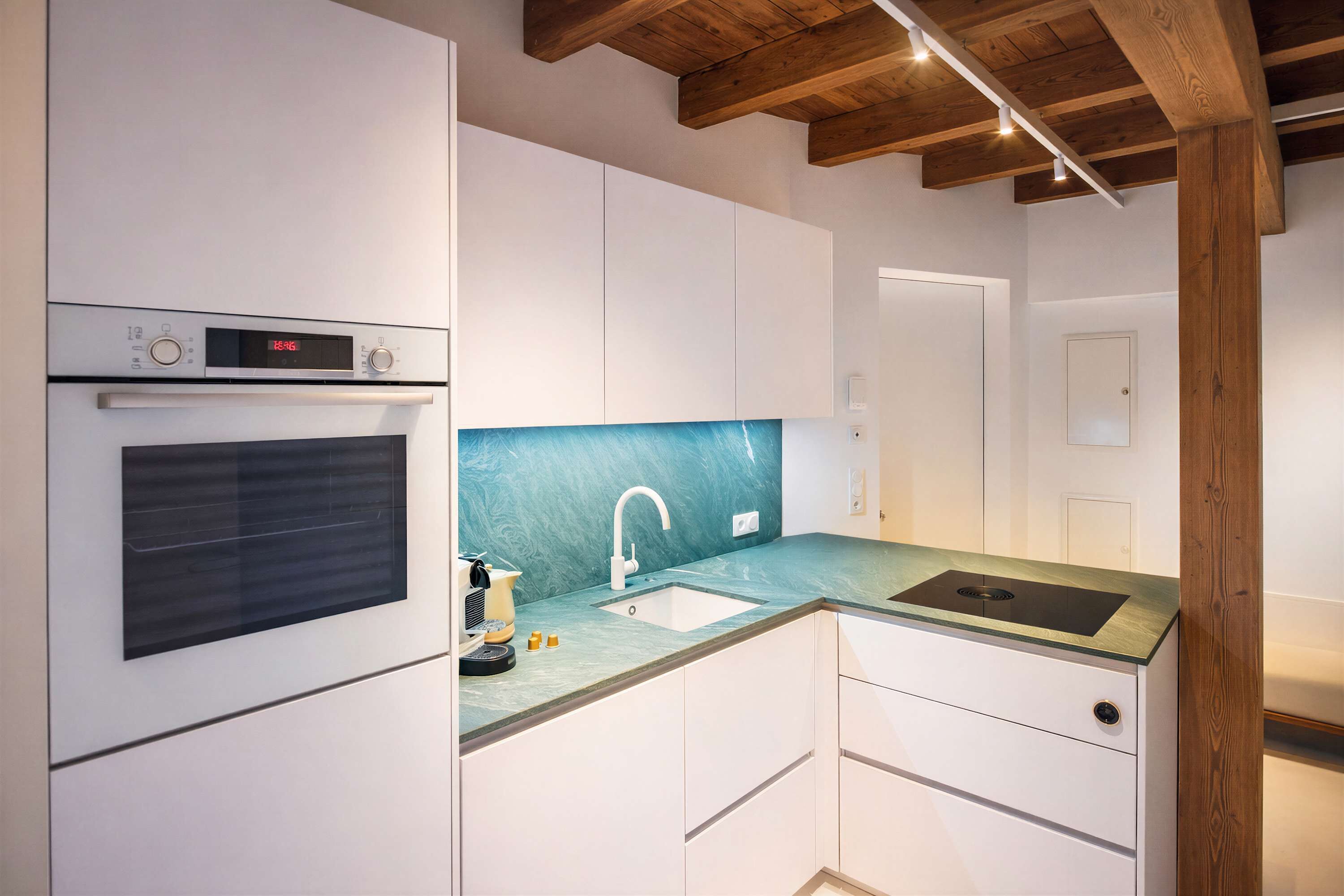 A modern kitchen with built-in appliances, a sink, and wooden ceiling beams.