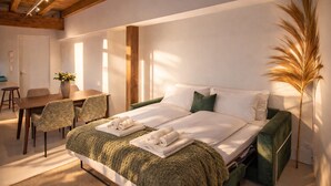 Quarto com cama, duas cadeiras, mesa e uma planta grande.