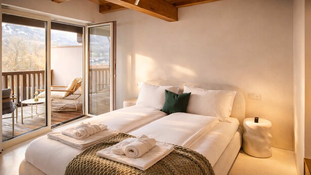 Quarto com cama grande, mesa de cabeceira, cadeira e varanda com vista.